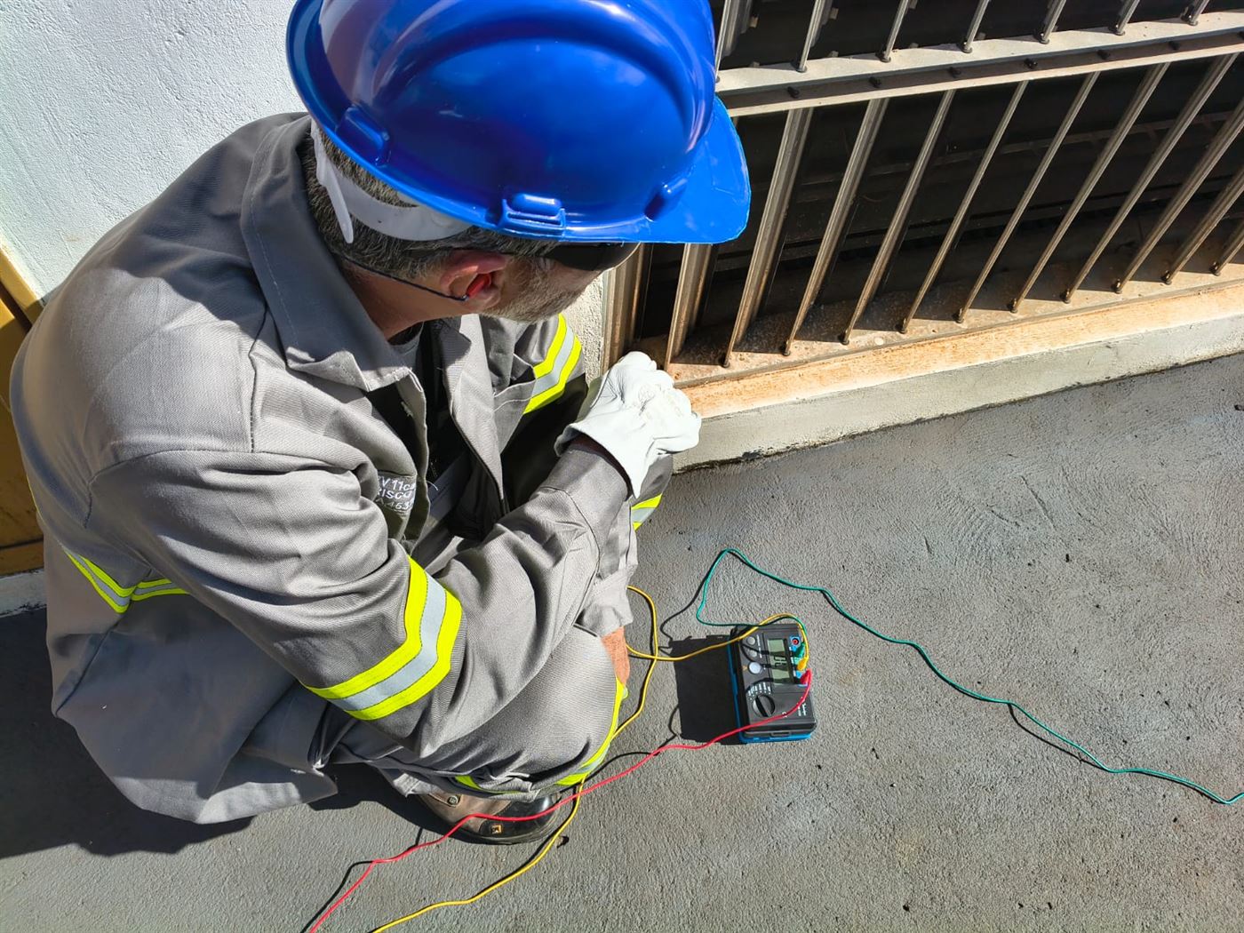 Profissional com EPI completo executando ensaio de aterramento junto à edificação